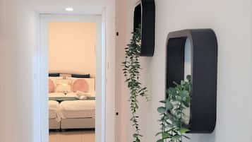 Een gang die leidt naar een slaapkamer met een bed, een aan de muur bevestigde televisie en een hangplant.