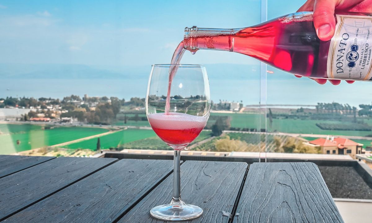 Une bouteille de vin Donato est versée dans un verre sur une table en bois, avec un paysage pittoresque en arrière-plan.