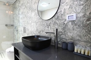 Un baño moderno con un lavabo tipo cuenco negro, un espejo redondo y una pared con estampado de mármol.