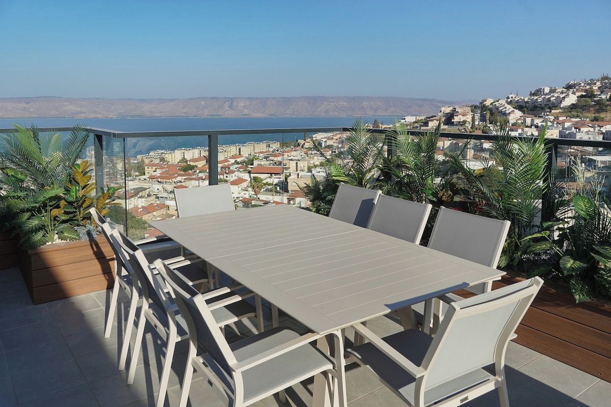 A terrace with a table and chairs, overlooking a coastal town.