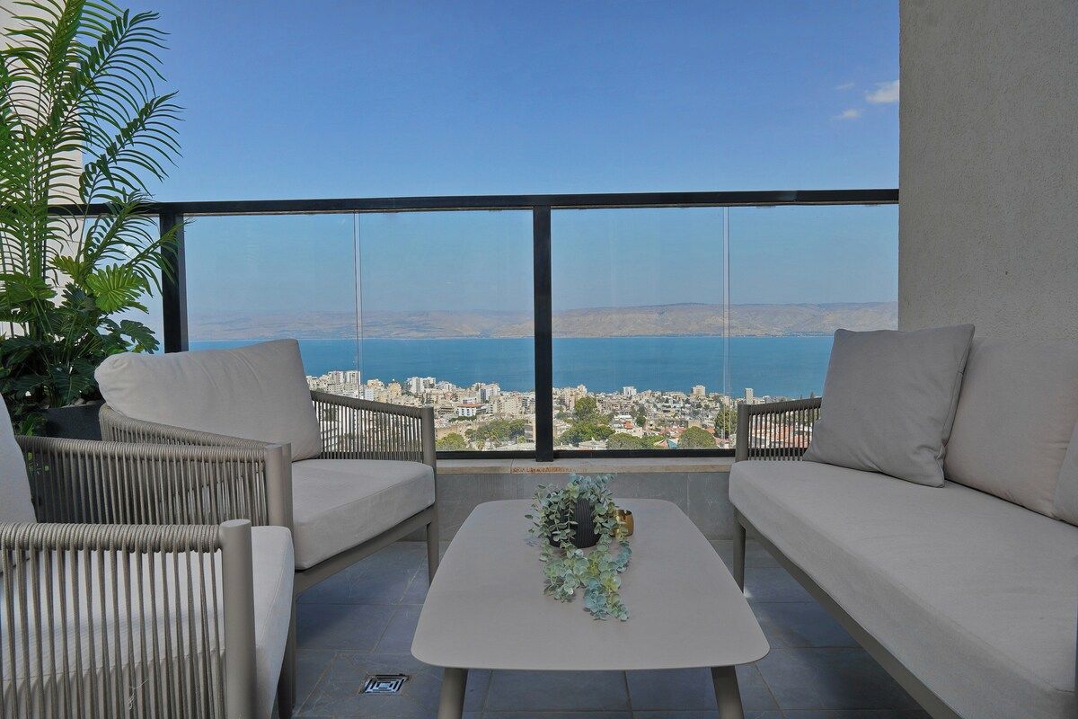 A balcony with a sofa, chairs, and a table, overlooking a city and body of water.