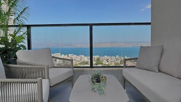 A balcony with a sofa, chairs, and a table, overlooking a city and body of water.