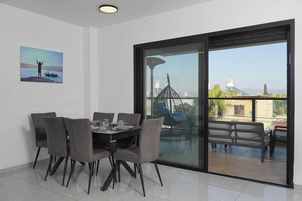 Een eetruimte met een tafel voor vier personen, een groot raam met uitzicht op een stadsbeeld en een schilderij aan de muur.