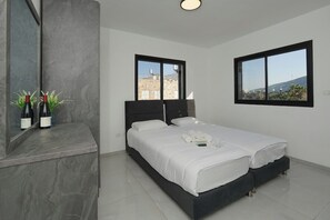 Une chambre moderne avec un grand lit, deux fenêtres, une table de chevet en marbre et une vue sur les immeubles.