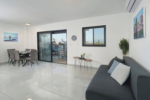 Un salon moderne comprenant un coin repas, un canapé, une table basse et une vue à travers une porte vitrée.