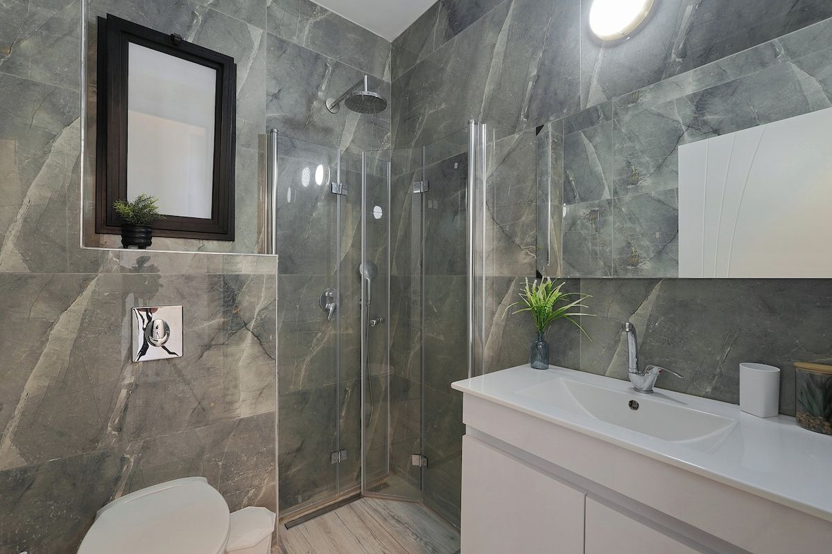Een moderne badkamer met een douchecabine van glas, een witte wastafel en een spiegel erboven.