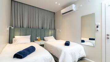 Une chambre d’hôtel avec deux lits, un grand miroir, un appareil de climatisation et une table de chevet avec une bouteille.