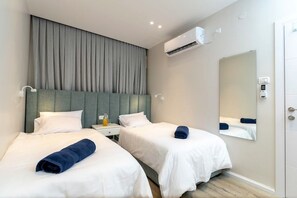Une chambre d’hôtel avec deux lits, un grand miroir, un appareil de climatisation et une table de chevet avec une bouteille.