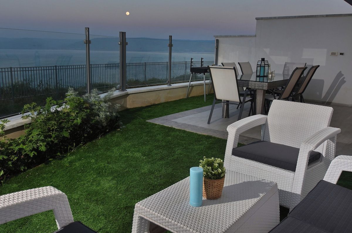 Een terras met tuinmeubilair, uitzicht op zee en een klein tuintje.