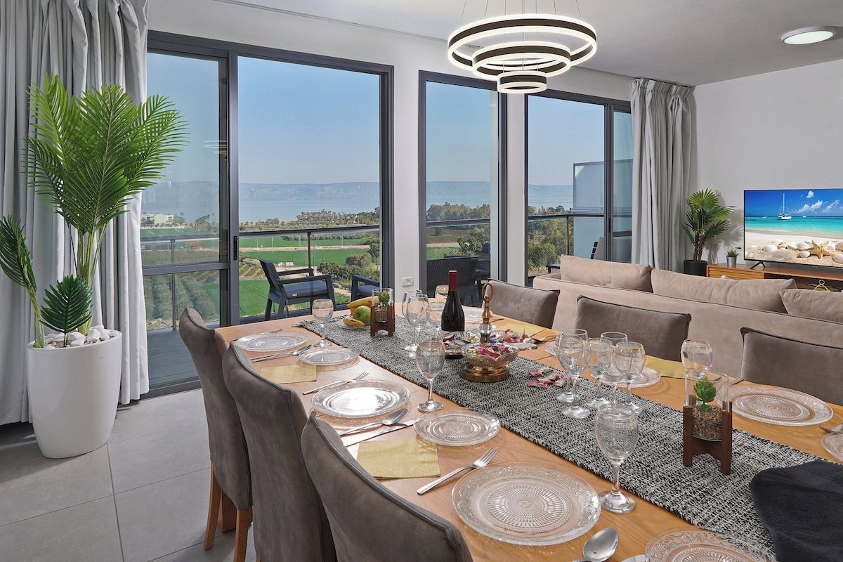Un coin repas avec une table dressée pour six personnes, de grandes fenêtres et une vue sur le paysage.