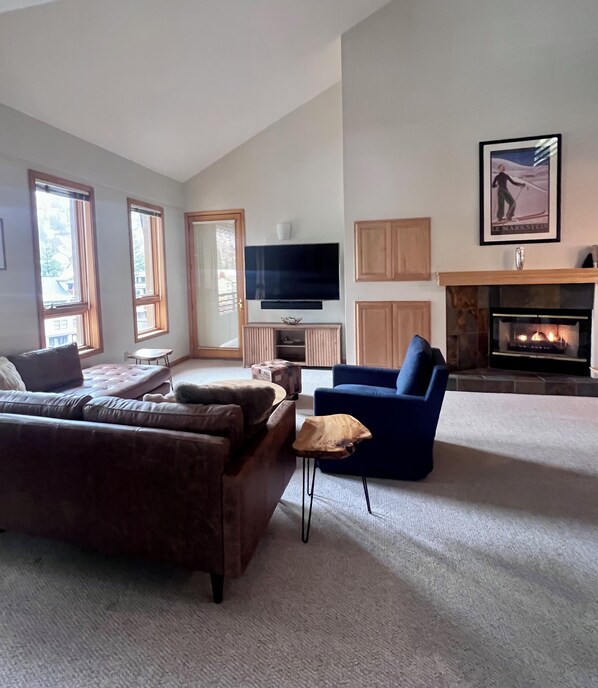Ein Wohnzimmer mit einer großen Couch, einem blauen Sessel, einem Fernseher und einem Kamin.