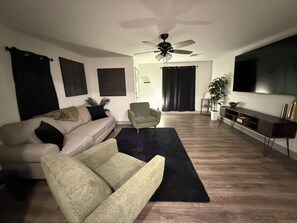 A living room with a sofa, armchair, and a flat-screen TV. - 3-bedroom house with relaxing character in a small quiet neighborhood. (Orange)