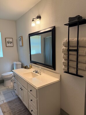 A bathroom with a white sink, a mirror, a towel rack, and a toilet. - 3-bedroom house with relaxing character in a small quiet neighborhood. (Orange)