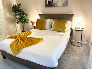 A neatly made bed with a white comforter and a yellow throw blanket, a bedside table with a lamp, and a potted plant. - Amazing Apt/nice pool/gym/free parking (Culver City)