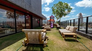 Un área de descanso al aire libre con asientos, una estructura de juegos infantiles y vistas panorámicas de la ciudad.