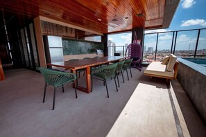 Una cocina moderna con techo de madera, una zona de comedor con sillas verdes y vistas a la ciudad a través de grandes ventanales.