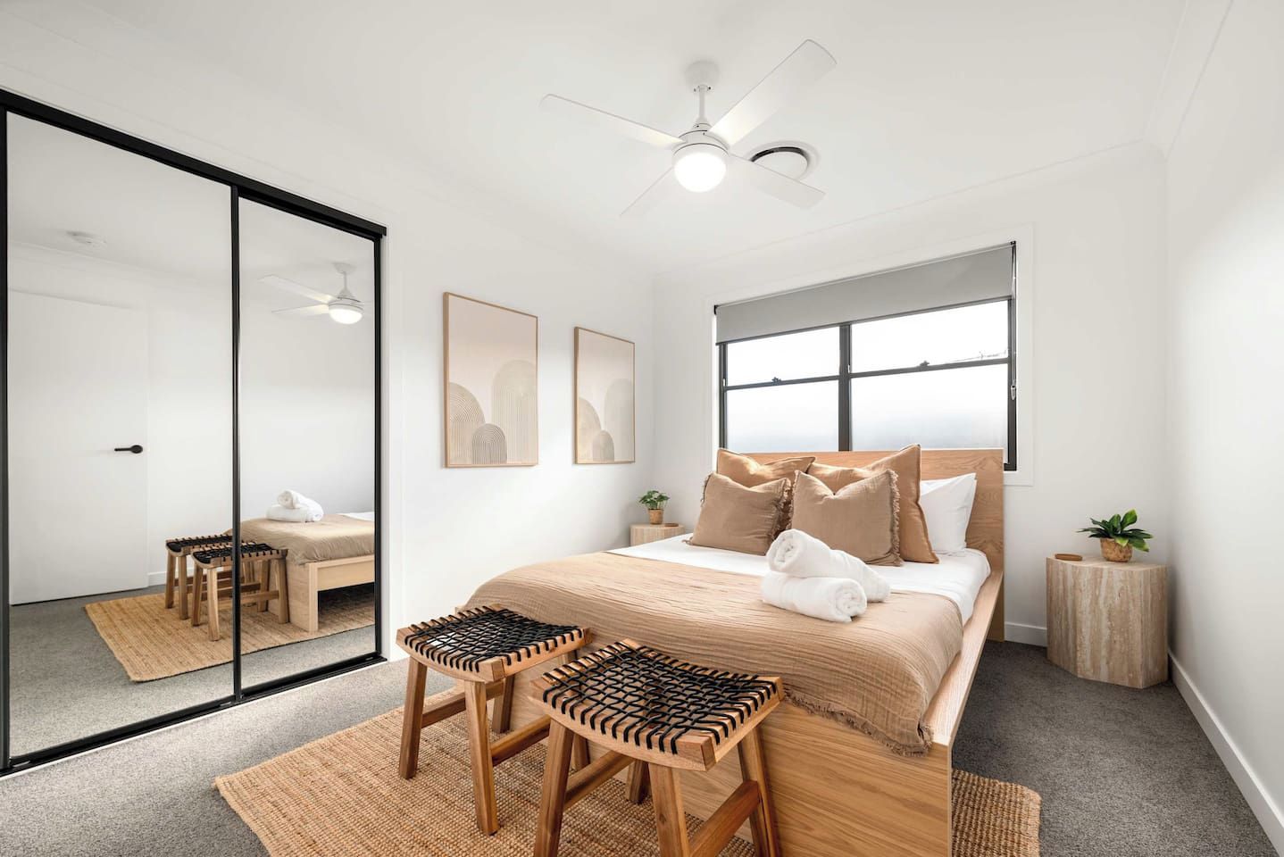 A modern bedroom with a bed, two chairs, a ceiling fan, and a large mirror.