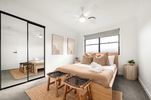 Un dormitorio moderno con cama, dos sillones, un ventilador de techo y un espejo grande.