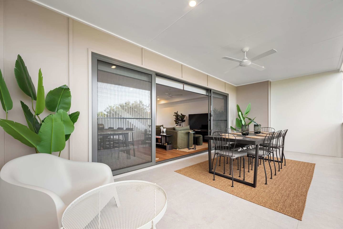 A modern interior with a dining area, white chairs, a table, and a large sliding glass door leading to an outdoor space.