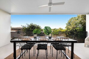 Un patio exterior con una mesa, sillas, ventilador de techo y vistas de la vegetación circundante.