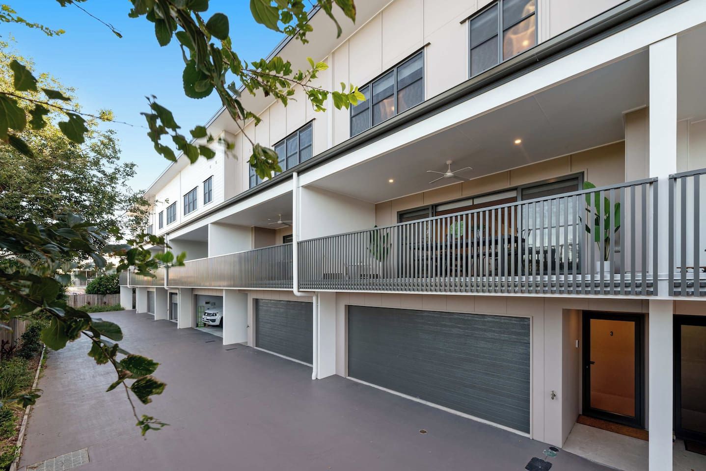 A modern multi-story residential building with balconies, garage doors, and a clear sky.
