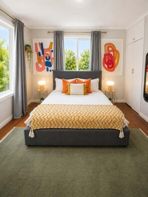 A bedroom with a large bed, two bedside tables, and a view of greenery outside. - Arty Beach Shack Deception Bay | Pets + Parking (Deception Bay)