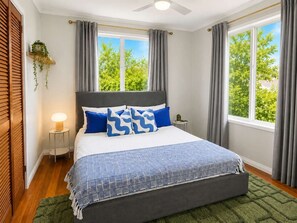A bedroom with a bed, a bedside table, a wall-mounted plant, and a window with curtains. - Arty Beach Shack Deception Bay | Pets + Parking (Deception Bay)