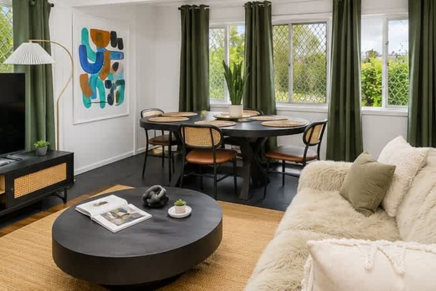 A living room with a round coffee table, a sofa, a dining table with chairs, a television, and a painting on the wall.
