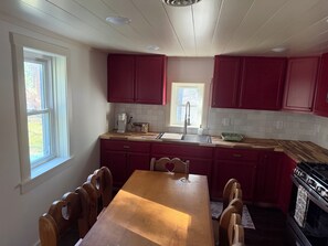 A kitchen with a wooden table, red cabinets, a window, and a stove. - Delightful 2-bedroom cabin in Vanderbilt perfect for a getaway (Vanderbilt)