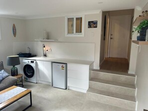 Un espacio habitable compacto con lavandería, un sofá pequeño, una mesa y una escalera que lleva a un piso superior.