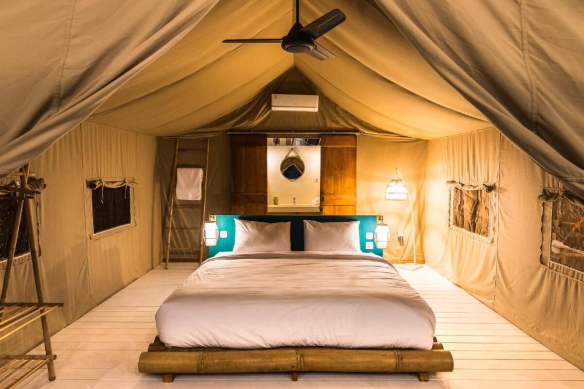 A tented room with a bed, a ceiling fan, a wall-mounted air conditioner, and two wall-mounted lights.