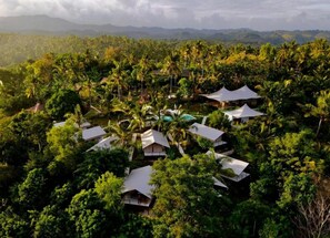 A resort with multiple bungalow-style accommodations surrounded by dense tropical vegetation and a mountainous backdrop. - Autentik Penida (Klungkung)