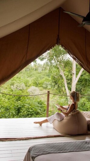 A tented room with a bed, a bean bag, and a person reading a book. - Autentik Penida (Klungkung)