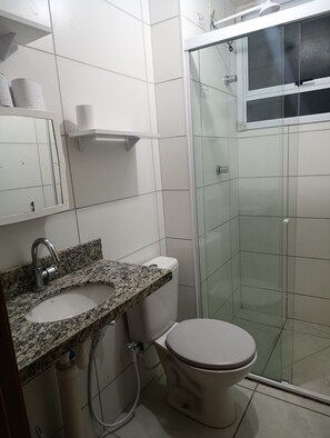 Un baño con lavamanos de encimera de granito, inodoro y ducha con mampara de vidrio.