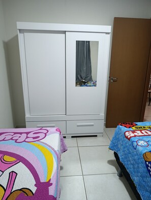 Un dormitorio con un armario blanco, una puerta de madera y dos camas con ropa de cama colorida.