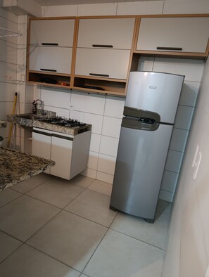 Una cocina con armarios blancos, un refrigerador de acero inoxidable, una encimera de granito y una estufa a gas.