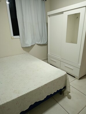 Una habitación con cama, armario y ventana con cortina.