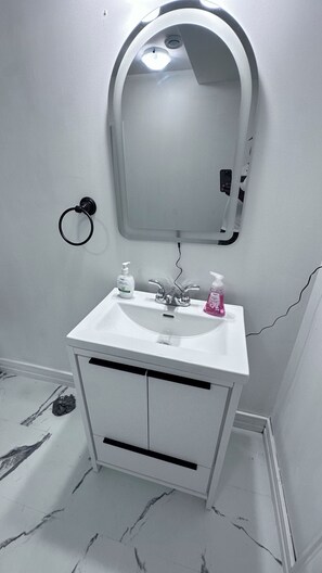 A bathroom with a white sink, a mirror, and a towel ring. - Creekside Haven Suite (Moncton)