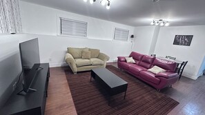 A living room with a flat-screen TV, a beige sofa, a red leather sofa, and a dark coffee table. - Creekside Haven Suite (Moncton)