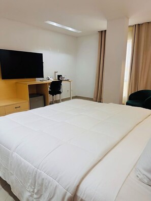 Une chambre d’hôtel avec un grand lit, un bureau avec une chaise, une télévision et une fenêtre avec des rideaux.