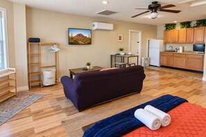 Una sala de estar con sofá, mesa de centro, televisor y área de cocina con armarios y refrigerador.