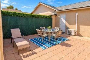 Un patio al aire libre con una mesa y sillas, una valla verde y un edificio color crema.