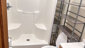 Kylpyhuone, jossa on kylpyamme, wc ja metallinen hyllykkö.