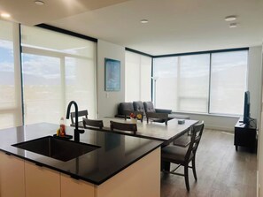 A modern kitchen with a central island, dining area with chairs, a sofa, and a TV. - DOWNTOWN LAKEVIEW LUXE 2BD apartment in marvelous Kelowna with AC and comfort (Kelowna)