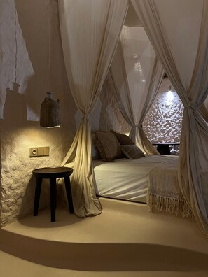 Ein Zimmer mit einem Bett, einem kleinen Hocker und einer Wandleuchte.