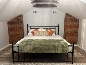 Un dormitorio con techo inclinado, una cama con manta verde y dos rejillas de ventilación visibles.