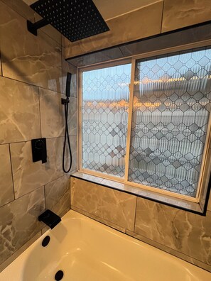 Un baño con bañera, ducha y ventana con diseño geométrico.