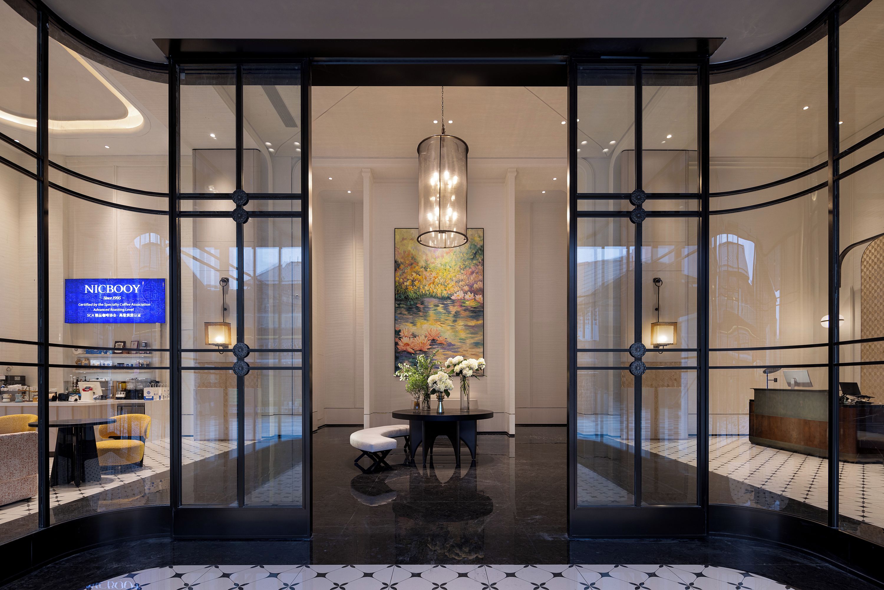 A modern hotel lobby with a reception desk, seating area, and a large window displaying a floral painting.