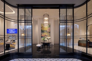 En moderne hotellobby med receptionsdisk, siddeområde og et stort vindue der viser et blomsterbillede.