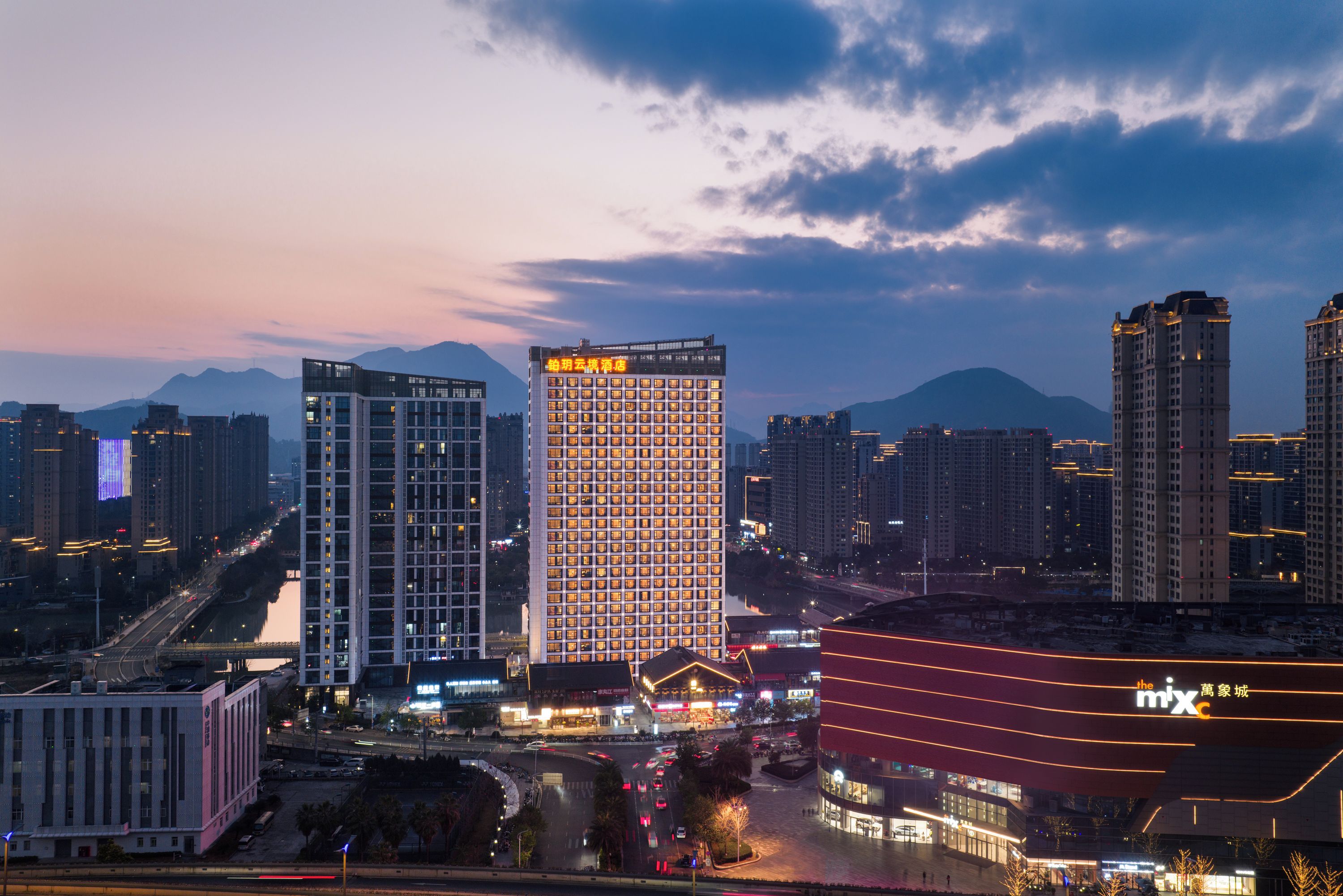 A high-rise hotel with a grid of windows, surrounded by other buildings and a mountain in the background.